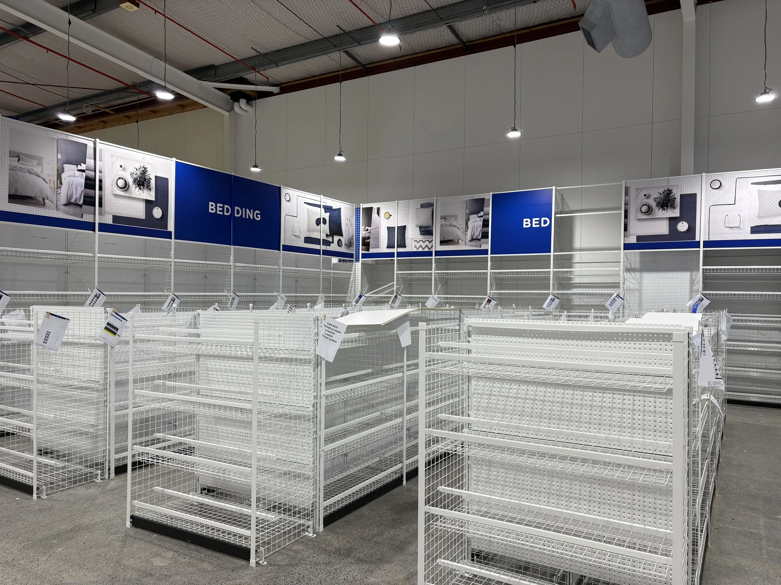 Empty retail floor with newly installed white shelving, overhead lighting and category graphics.