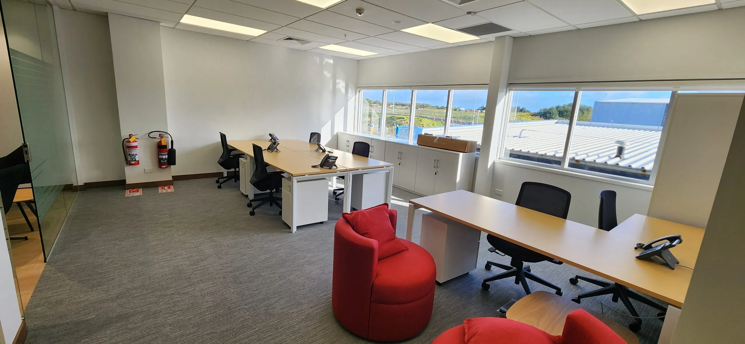 Completed open office with desks, task chairs, a red lounge chair and windows along the far wall.