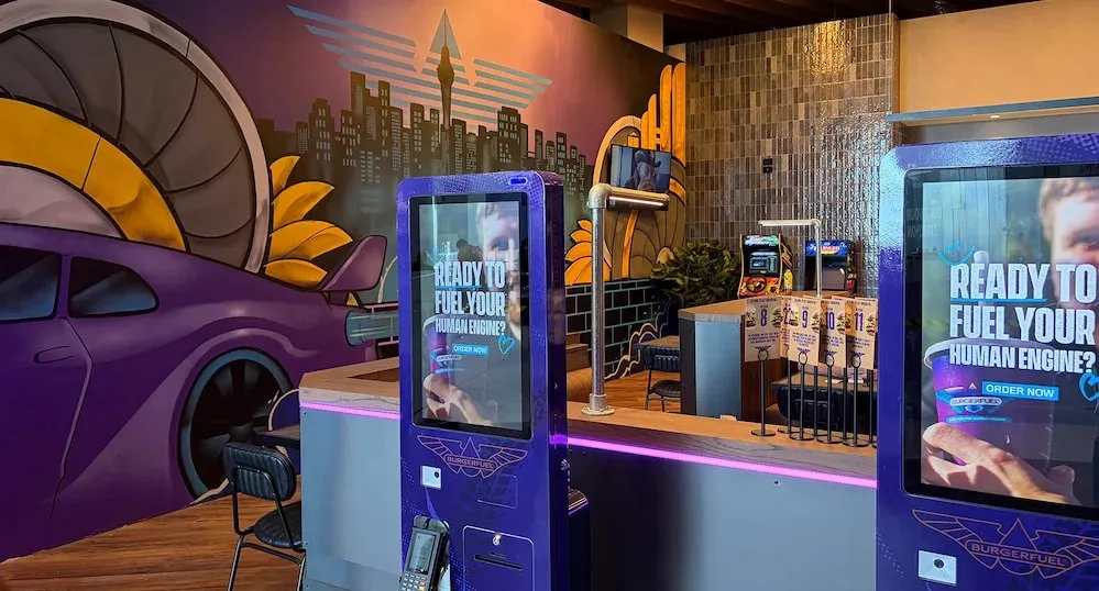 BurgerFuel service counter with order kiosks, a mural and the pass at Auckland Airport.