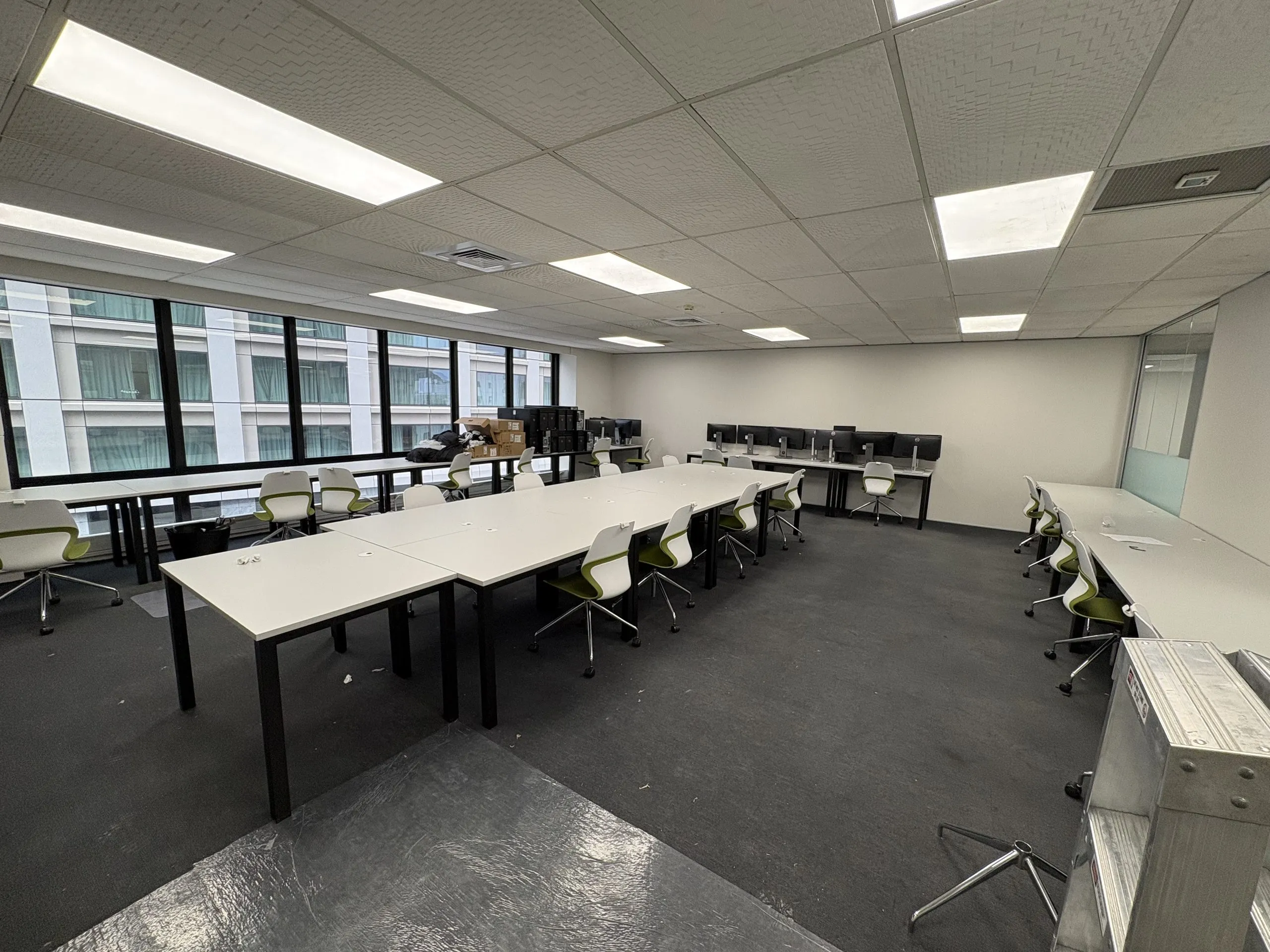 Learning room with installed tables, chairs and a row of computer monitors along the window.