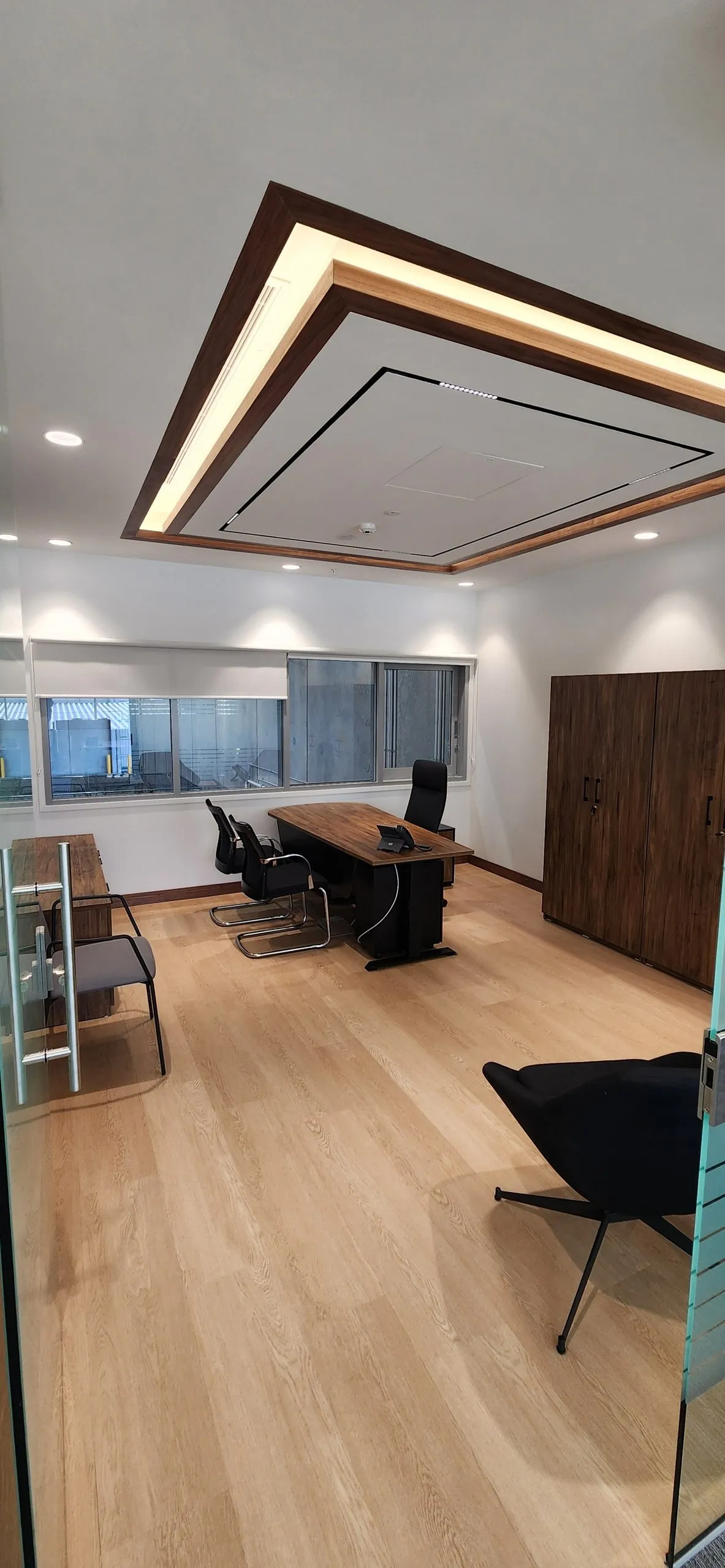 Private office with a timber desk, chairs, a timber cupboard and a rectangular ceiling light.