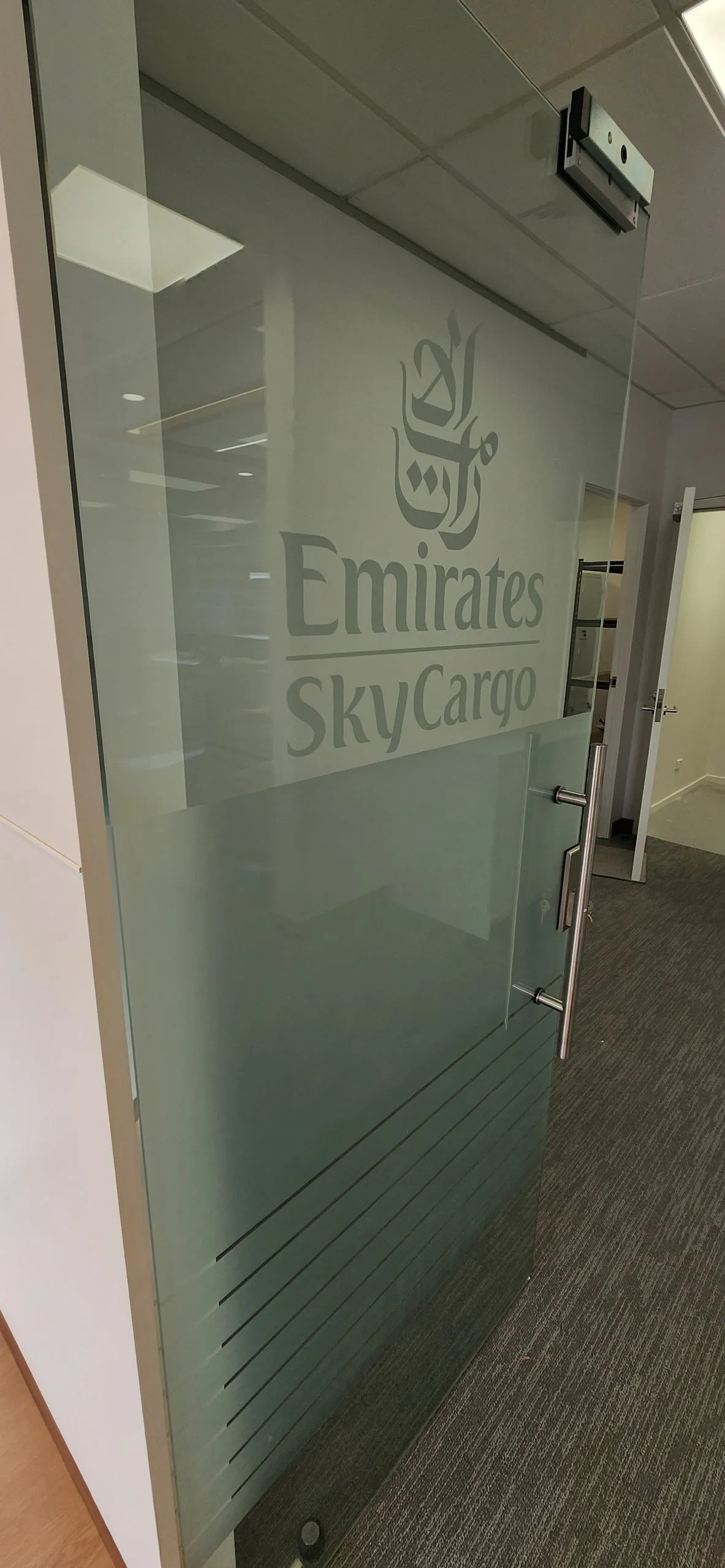 Glass door with Emirates SkyCargo lettering, a metal handle and frosted bands.