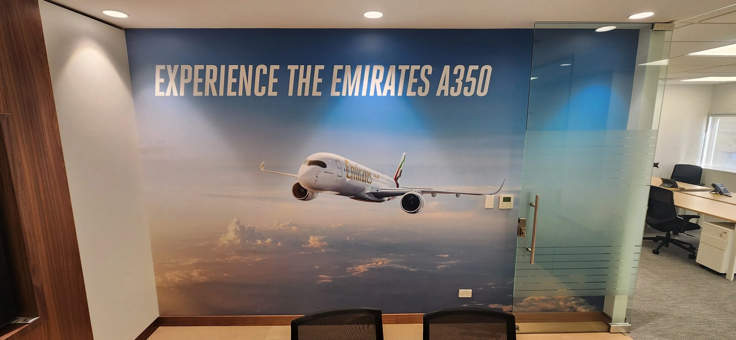 Branded glass partition beside a wall graphic reading Experience the Emirates A350.