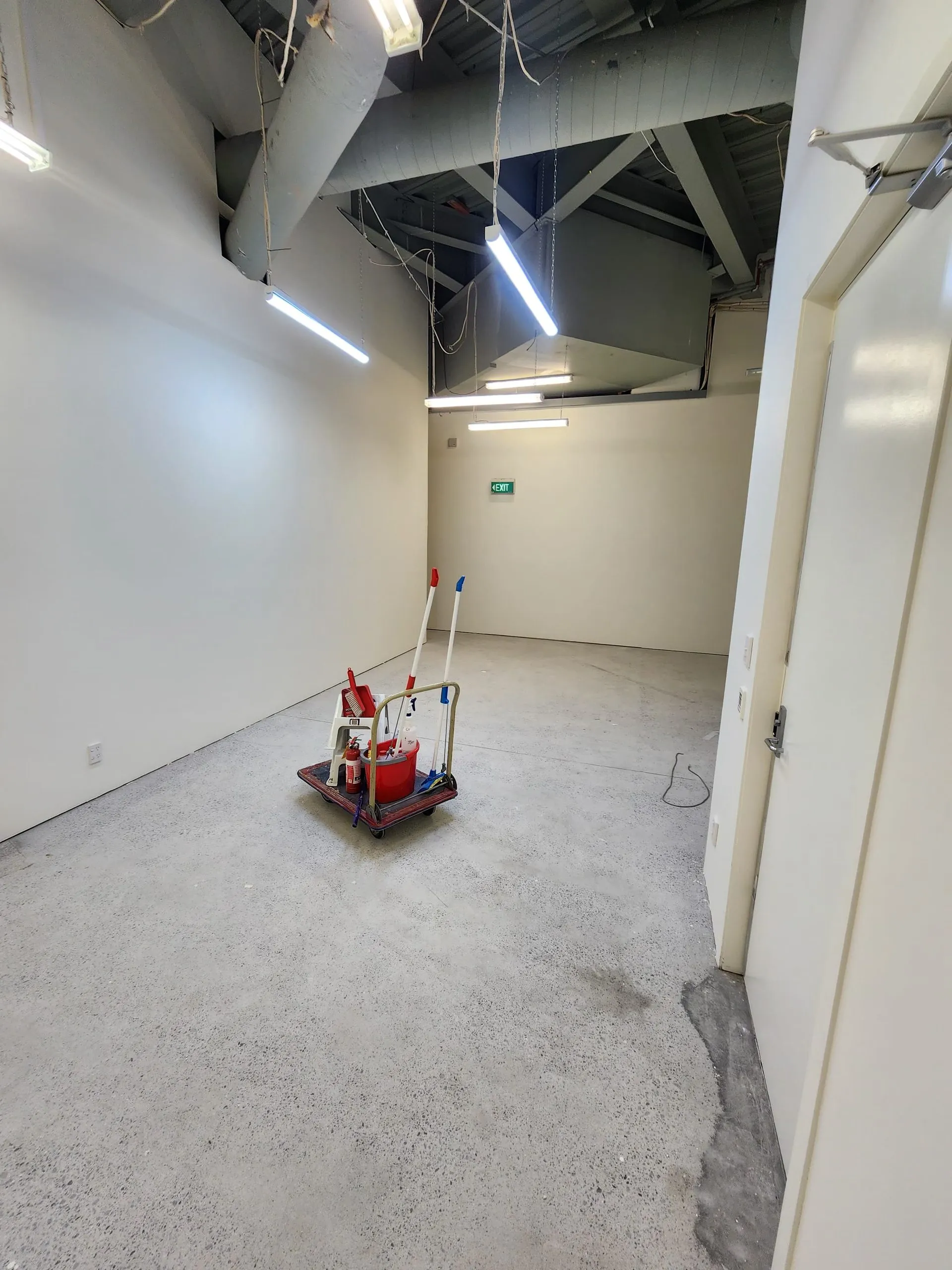 Cleared back-of-house room after strip-out, with an empty floor and remaining wall and ceiling services.