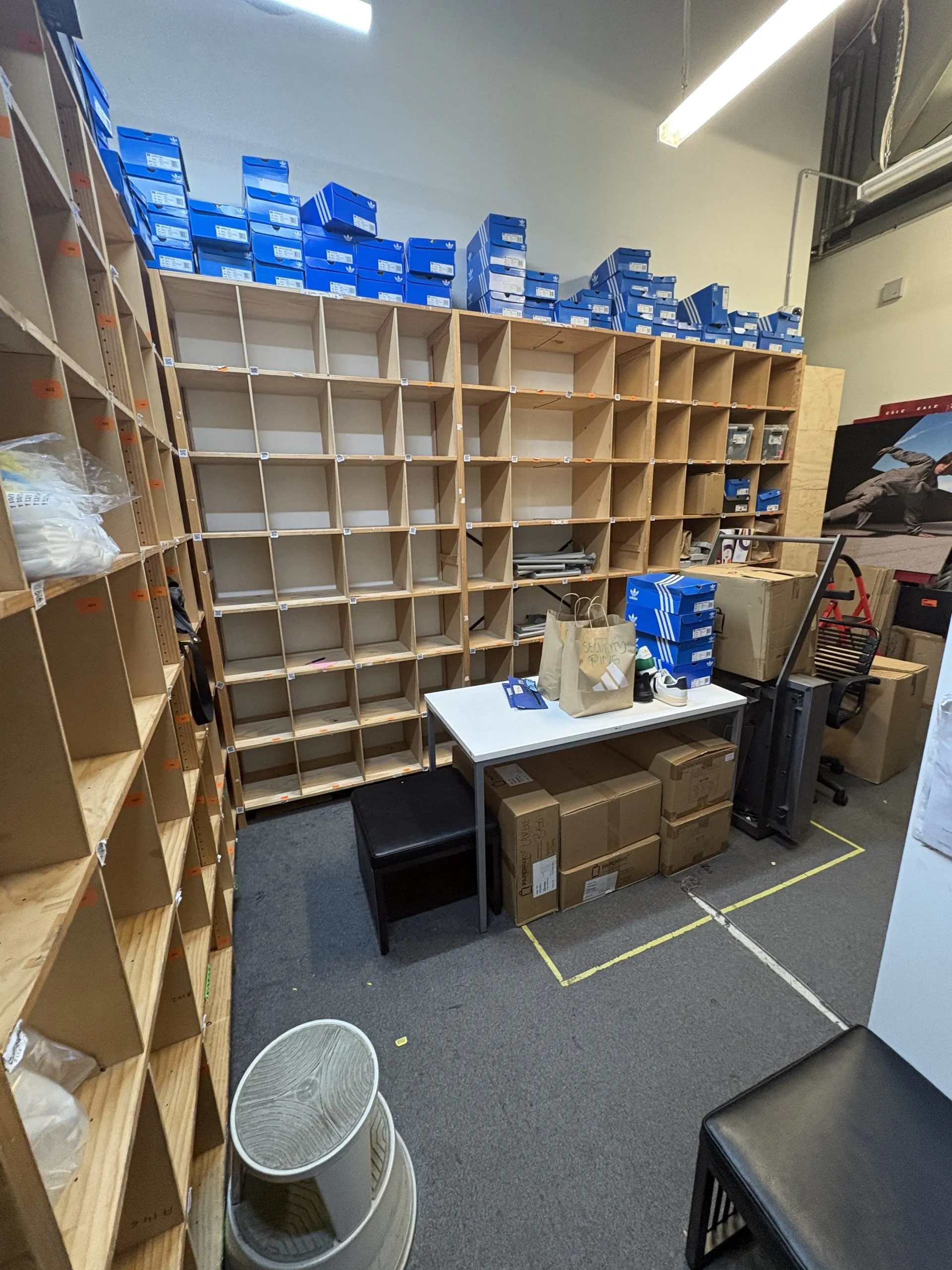 Back-of-house stock room before strip-out, with timber shelving, shoe boxes and packed goods.