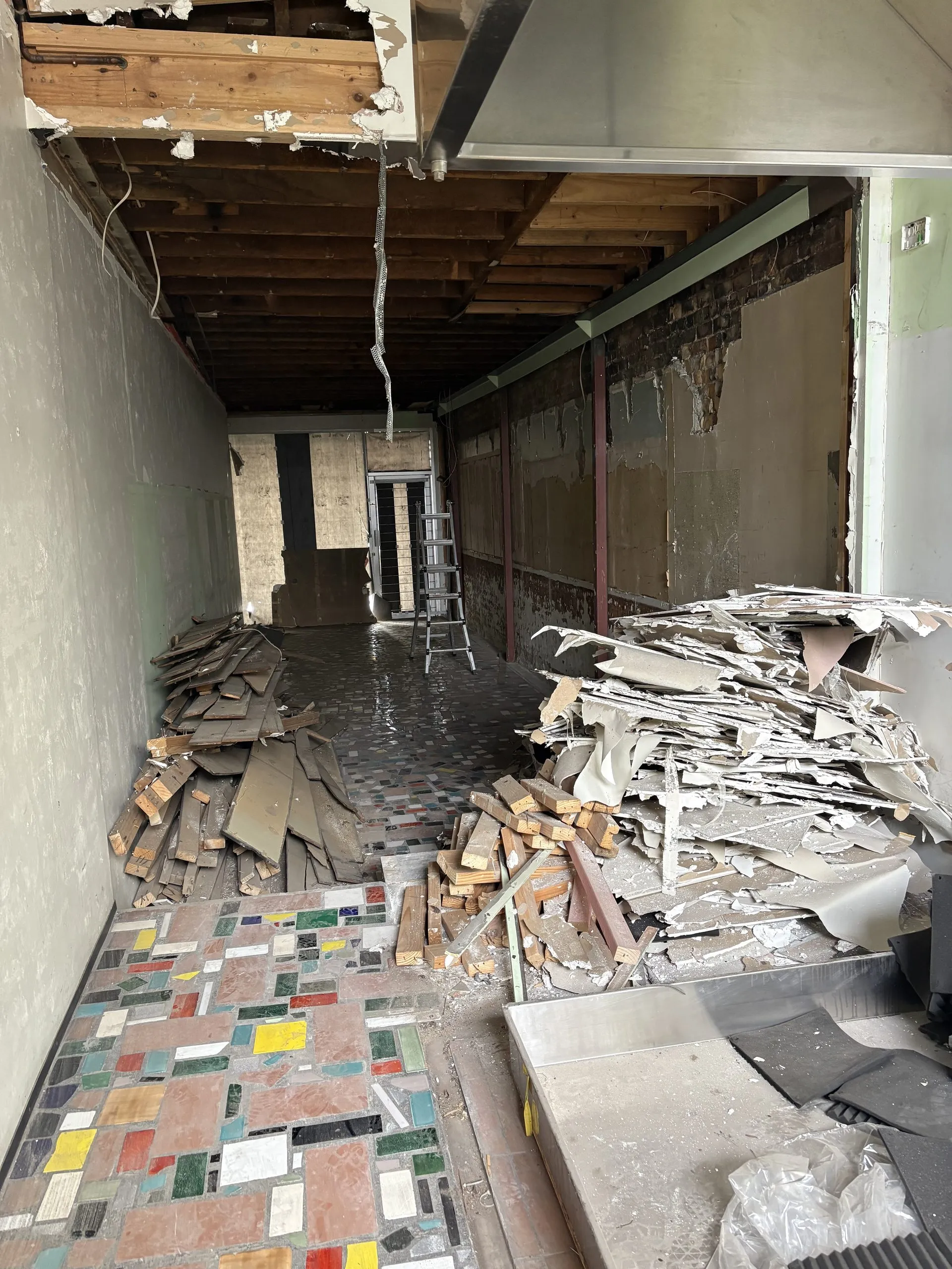 Strip-out corridor with exposed ceiling joists, removed wall linings and stacked debris.