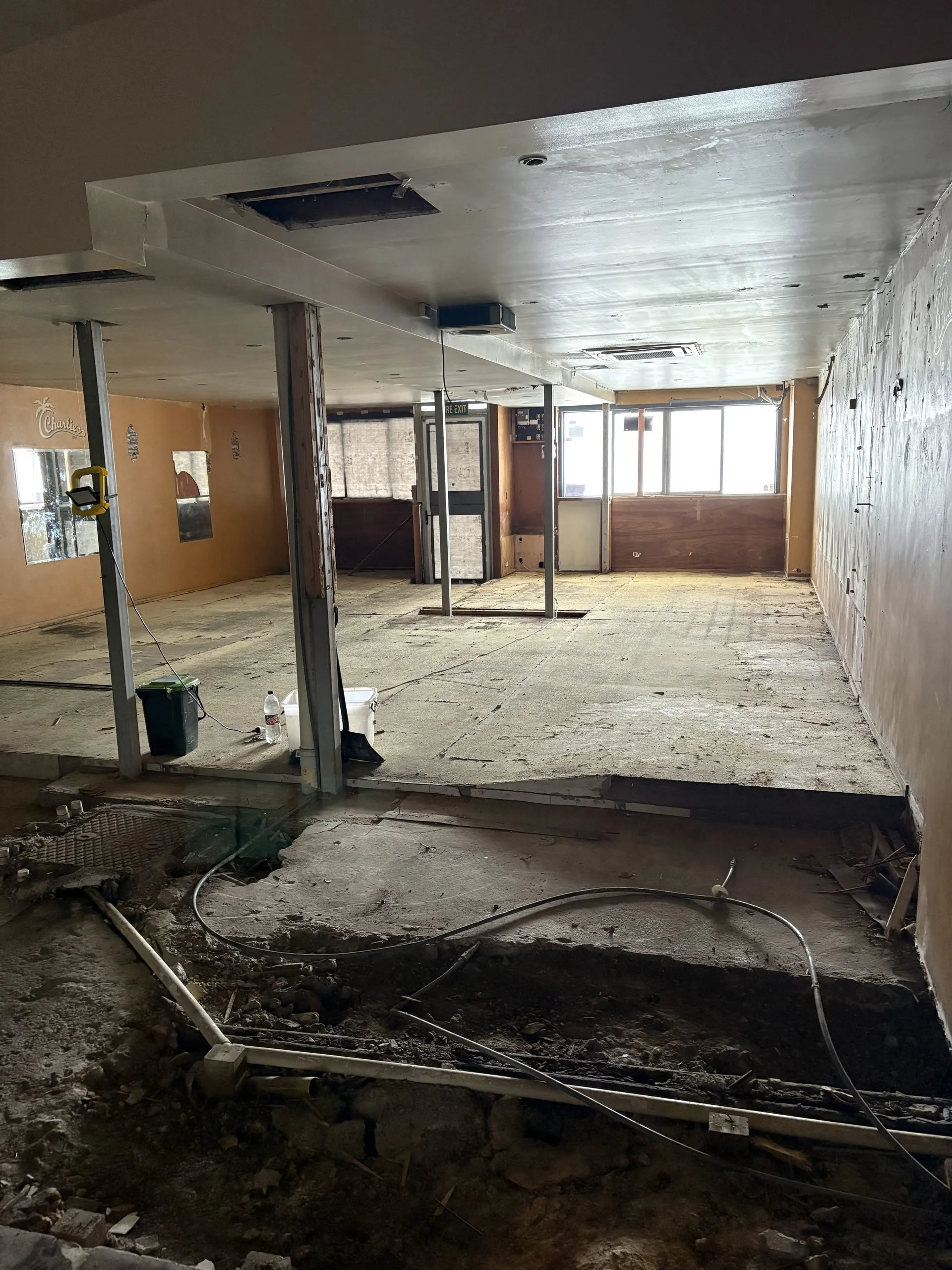 Cleared commercial room during strip-out, with exposed ceiling services, remaining partitions and an opened floor.